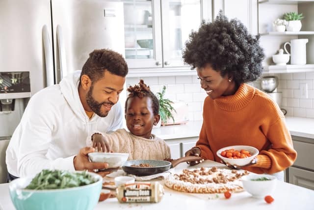 Small family of people of color, a son, a mother, and a father, smiling and enjoying lunch in their home kitchen.