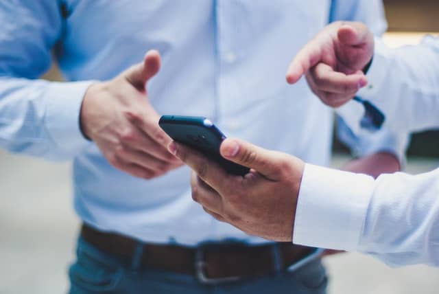 Two men in suits, one is holding a phone in his left hand. Both are pointing at something on the screen.