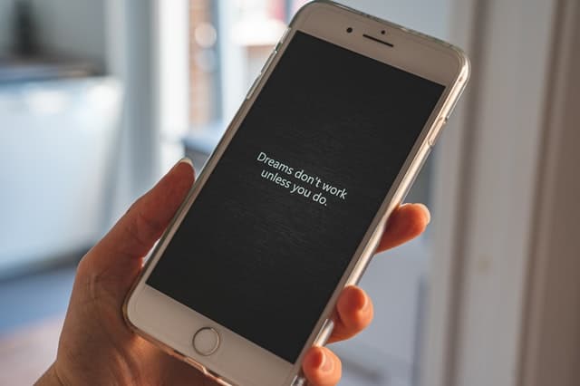 A hand holding a phone, with an image of a wooden background and a text quote on top saying "dreams don't work unless you do".